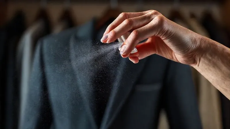 photorealistic, professional photography, 8K, cinematic lighting, sharp focus, depth of field, shot on a high-end DSLR, a hand gently misting a very fine, almost invisible spray of perfume onto a crisp, clean blazer. The background is a softly blurred, sophisticated office wardrobe, emphasizing care and precision in personal grooming. The focus is on the delicate application, suggesting subtlety and restraint.