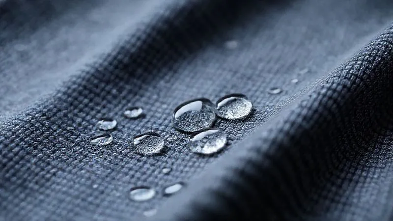 Photorealistic, professional photography, 8K, cinematic lighting, sharp focus, depth of field, shot on a high-end DSLR. A macro shot of a high-performance activewear fabric, showcasing its intricate weave and texture. Droplets of water are beading on the surface, demonstrating moisture-wicking properties. The fabric has a soft, almost brushed appearance, with subtle stretch visible.