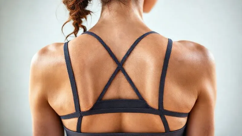 Photorealistic, professional photography, 8K, cinematic lighting, sharp focus, depth of field, shot on a high-end DSLR. A close-up, detailed shot of the back of a woman wearing a well-designed yoga bra. The focus is on the intricate strap design (e.g., cross-back, racerback, wide adjustable straps) that evenly distributes weight across her shoulders and back, showing no signs of digging in or chafing. Her skin looks smooth and comfortable beneath the fabric.
