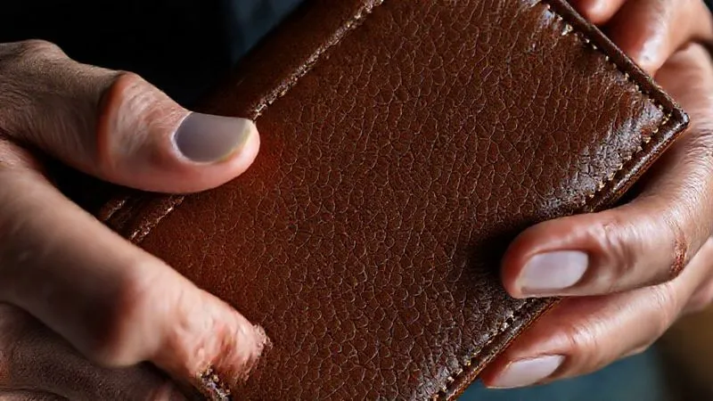 photorealistic, professional photography, 8K, cinematic lighting, sharp focus, depth of field, shot on a high-end DSLR, a close-up of a meticulously crafted luxury leather wallet, with a subtle, almost imperceptible metallic strip woven into the stitching, indicating hidden smart technology, the leather grain perfectly visible, hands gently holding the wallet, emphasizing tactility.