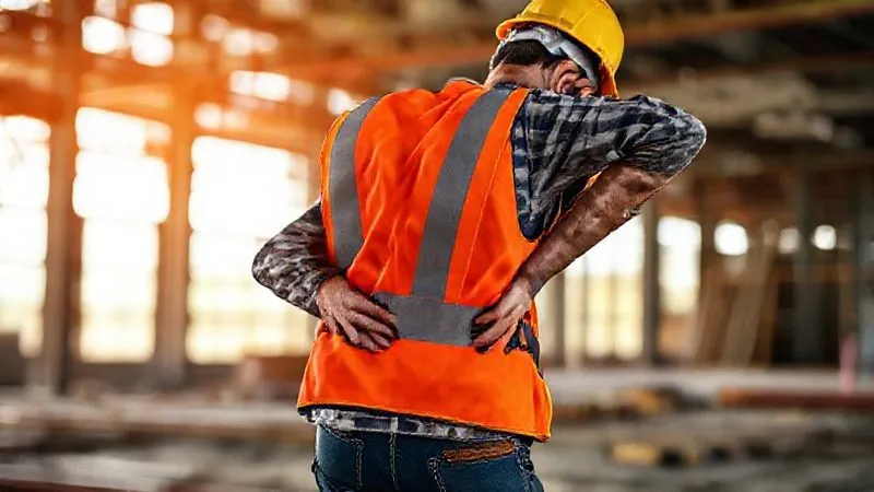 A photorealistic image of a construction worker in a hard hat and safety vest, subtly performing a gentle lower back stretch during a short break on a job site, with ergonomic work boots visible. Professional photography, 8K, cinematic lighting, sharp focus, depth of field, shot on a high-end DSLR, conveying relief and proactive self-care.